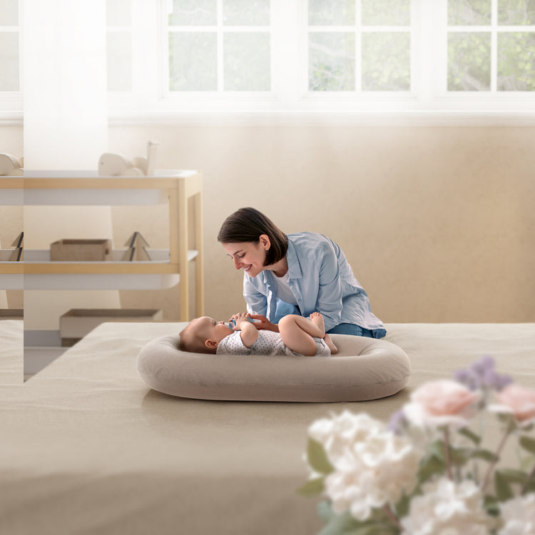 Woman and baby on a bed with a circular cushion in a bright room.