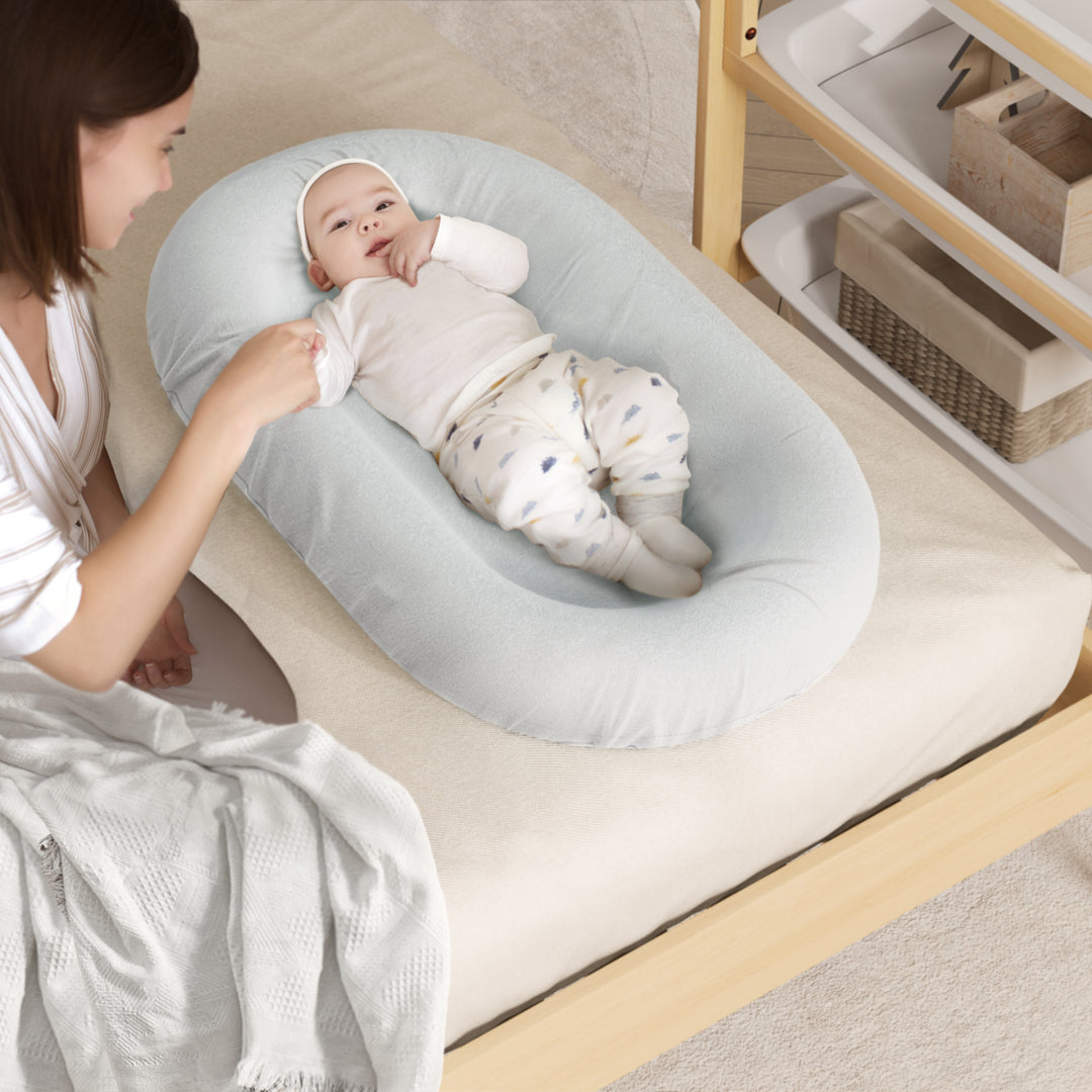 Woman adjusting a baby in a gray baby bouncer on a wooden floor.