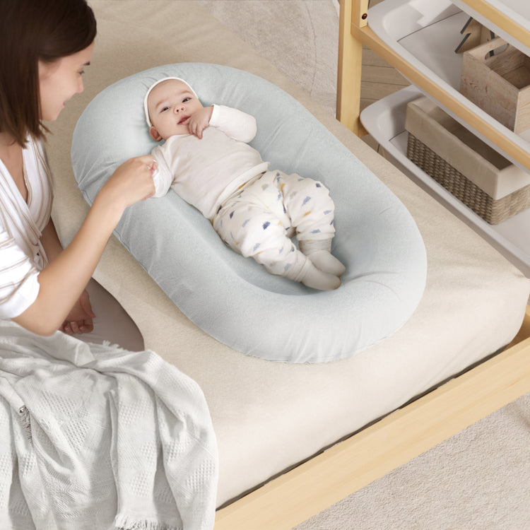 Woman adjusting a baby in a gray baby bouncer on a wooden floor.