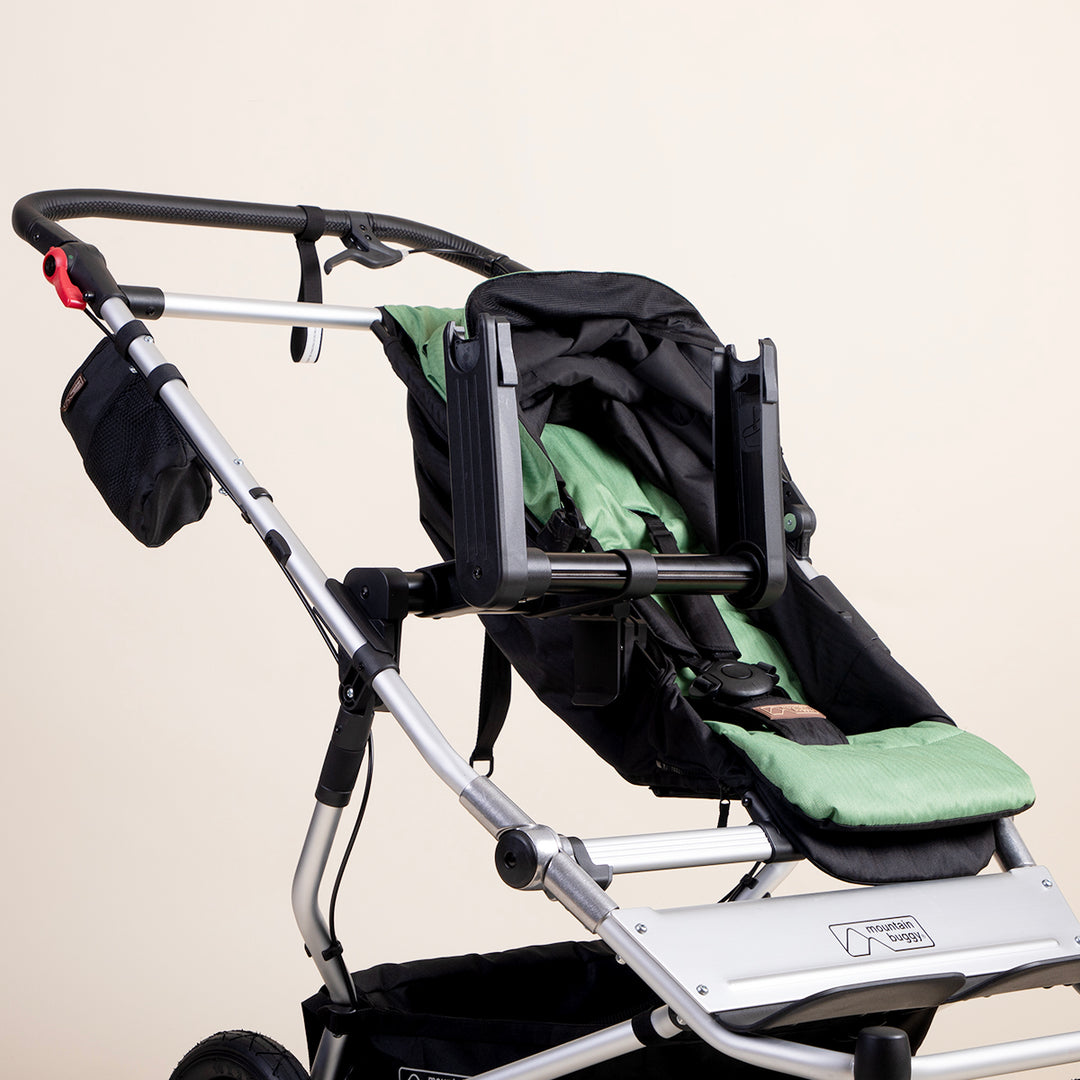 mid shot of a mountain buggy duet with a car seat adaptor installed alongside the standard buggy seat in matcha green on a white background