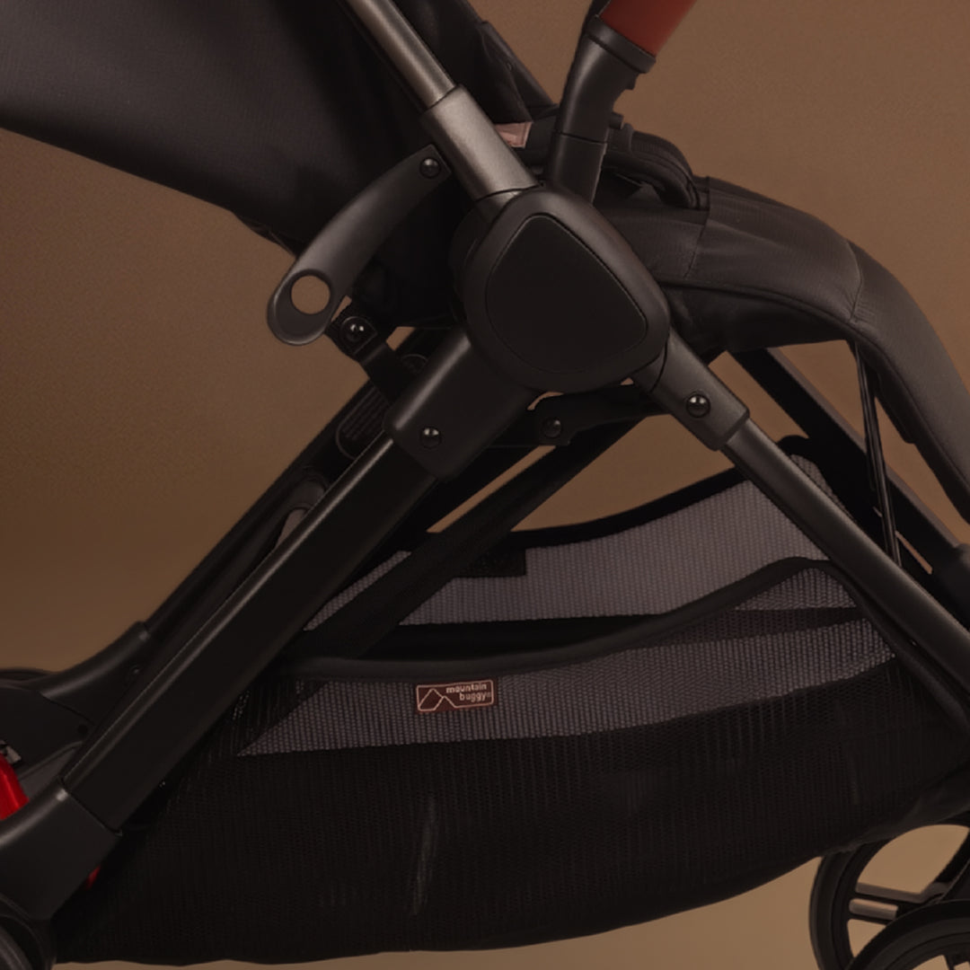 Close up of the Mountain Buggy nano urban in black shown against a brown background showing the storage tray and frame