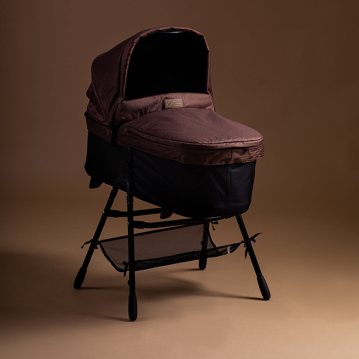 Full shot of the Mountain Buggy urban jungle carrycot plus in mustang brown on the stand accessory shown on a brown background
