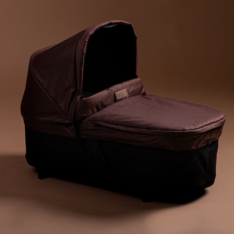 Full shot of the Mountain Buggy urban jungle carrycot plus in mustang brown shown on a brown background