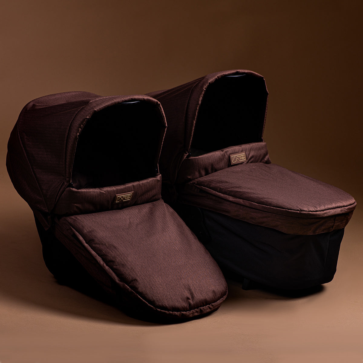 Full shot of Mountain Buggy carry cot plus in toddler mode and bassinet side by side in mustang brown on brown background
