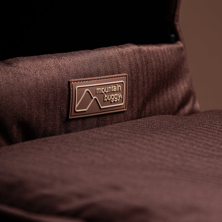 close up shot of Mountain Buggy carry cot plus showing logo on mustang brown colour option with brown background