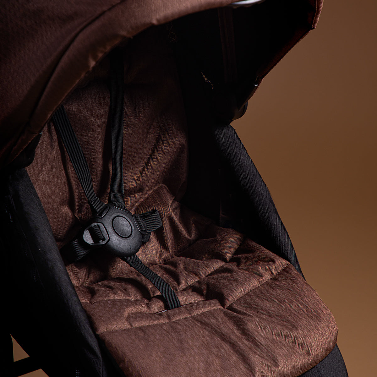 Close up shot of Mountain Buggy carry cot plus in mustang brown showing toddler seat and safety straps on brown background