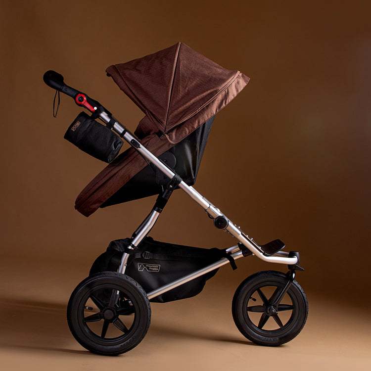 Full shot of the Mountain Buggy urban jungle carrycot plus in mustang brown in use on the urban jungle buggy shown on a brown background