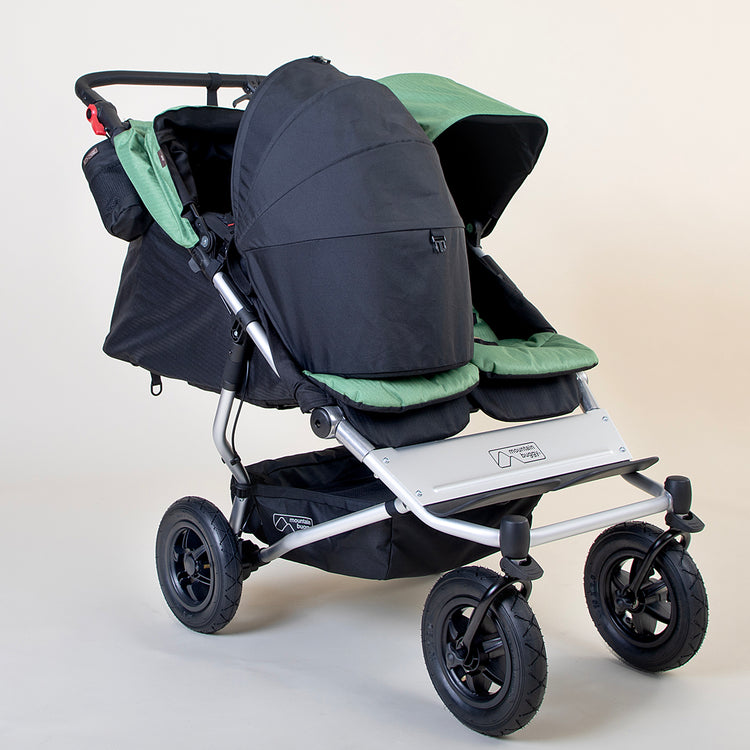 Full shot of Mountain Buggy duet in matcha green with front facing and bassinet + sunshade setup on a white background