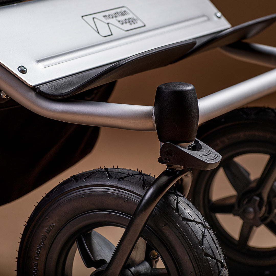 Close-up of a Mountain Buggy Duet front wheels and logo bumper on a brown background
