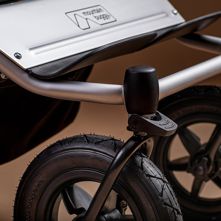 Close-up of a Mountain Buggy Duet front wheels and logo bumper on a brown background