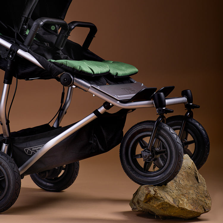 Full shot of Mountain Buggy duet in matcha green with both front wheels mounted on a rock on brown background