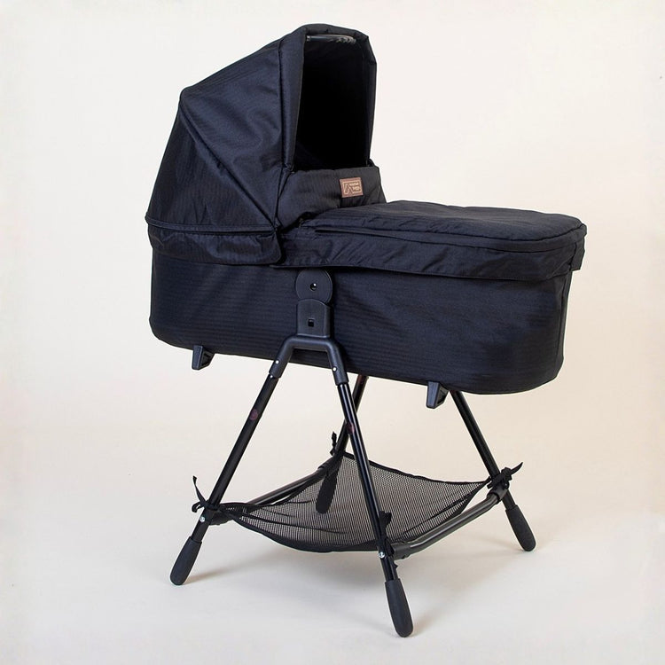 Full shot of Mountain Buggy carry cot plus for duet in caviar black with stand on white background