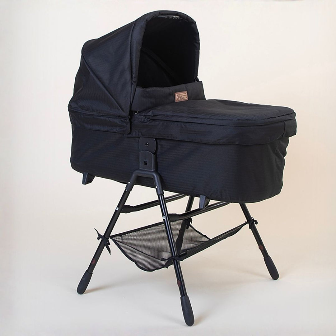 Full shot of the Mountain Buggy urban jungle carrycot plus in caviar black on the stand accessory on a white background 