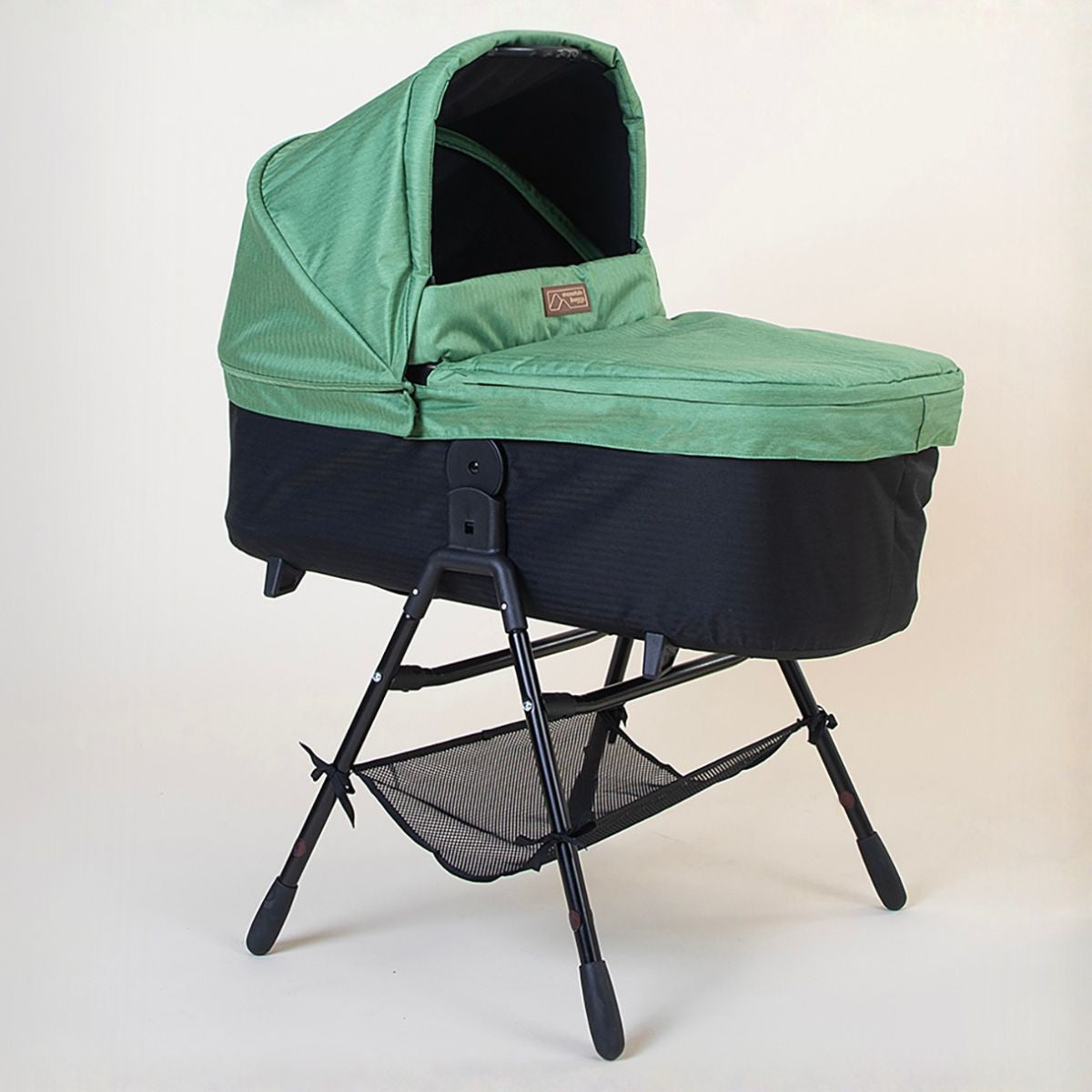 Full shot of the Mountain Buggy urban jungle carrycot plus in matcha green on the stand accessory on a white background 