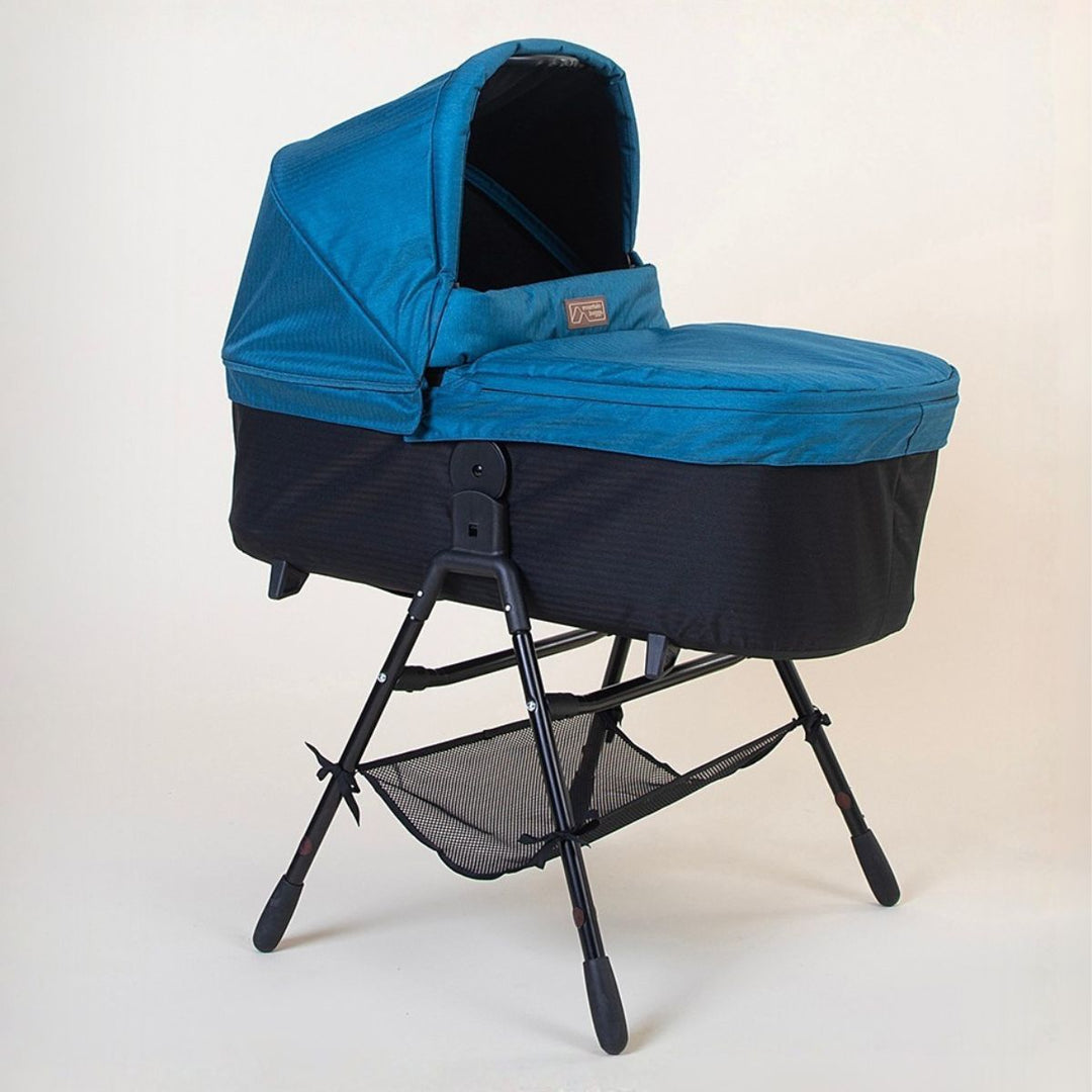 Full shot of the Mountain Buggy urban jungle carrycot plus in ocean blue on the stand accessory on a white background 
