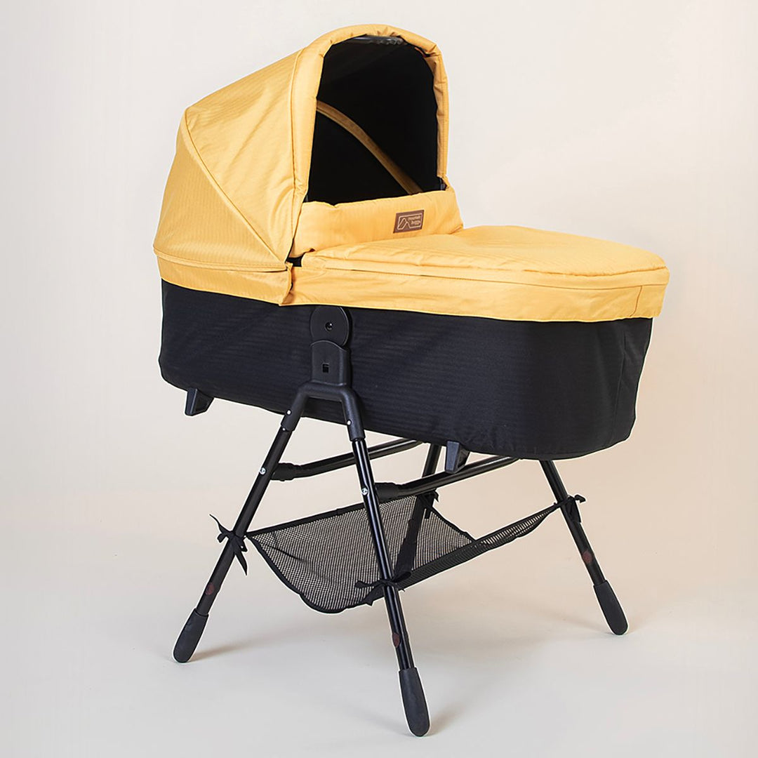 Full shot of the Mountain Buggy urban jungle carrycot plus in solare yellow on the stand accessory on a white background 