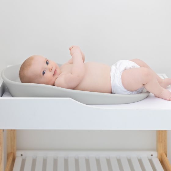Baby lying on a babyfirst change mat ontop of a changing table with a neutral background