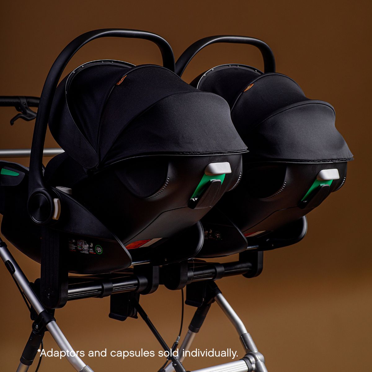 Mid shot of a mountain buggy duet with dual car seat adaptors and capsules fitted on a brown background