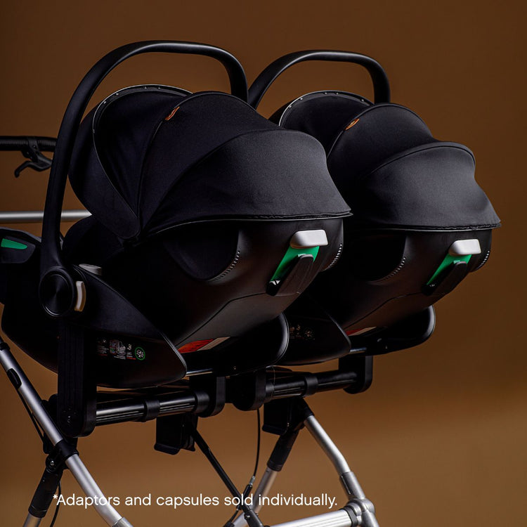 Mid shot of a mountain buggy duet with dual car seat adaptors and capsules fitted on a brown background