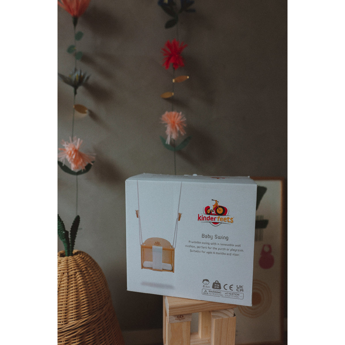 Kinderfeets baby swing packaging on a stand with decorative elements in the background