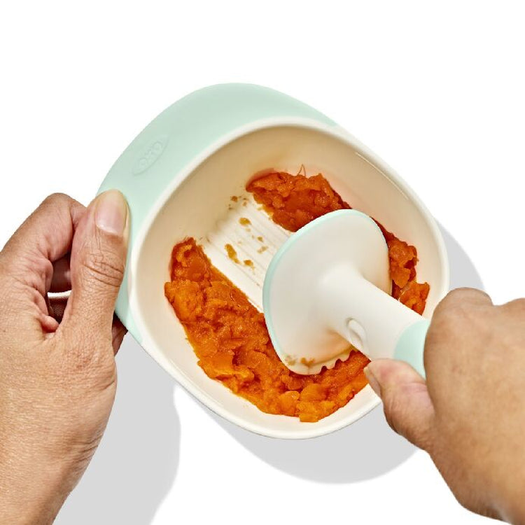 Person using a baby food puree container with a spoon filled with orange baby food.