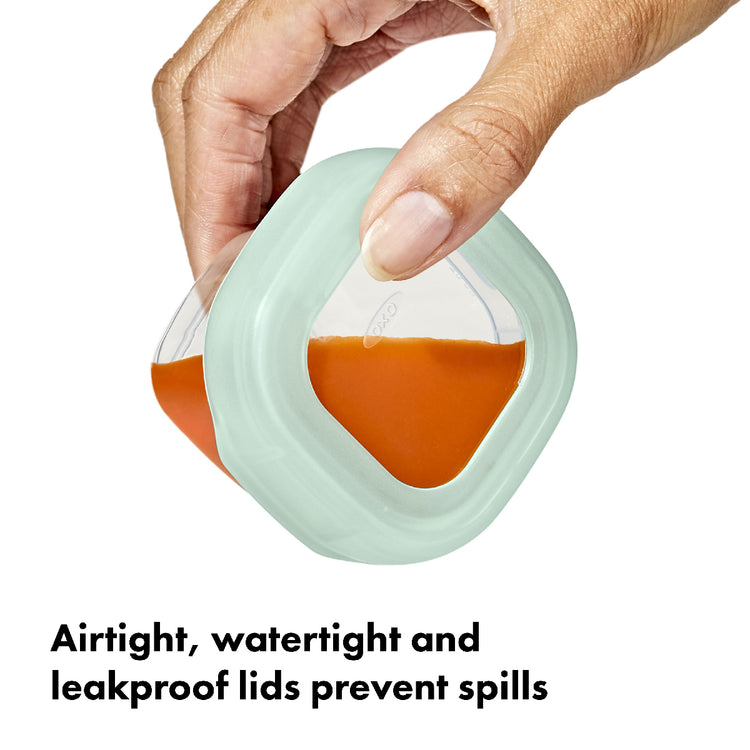 Hand holding a container with a green lid, filled with orange liquid, on a white background.
