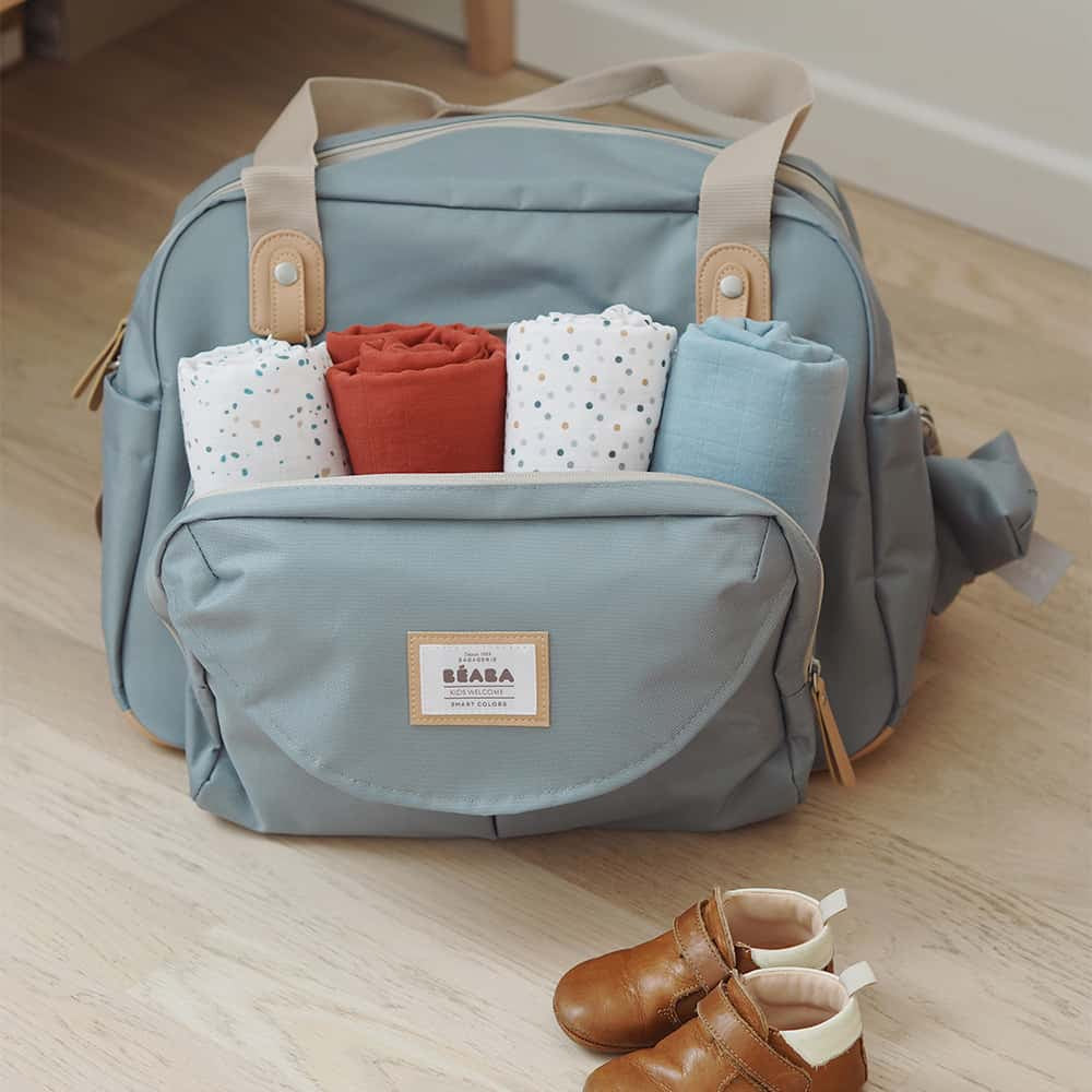 Light blue diaper bag with baby clothes and shoes on a wooden floor