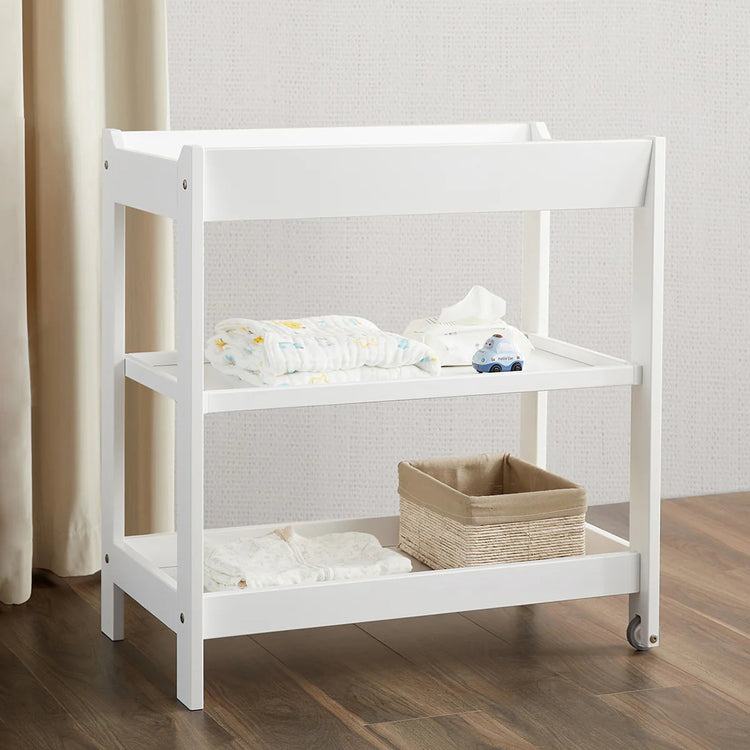 White baby changing table with a basket and folded clothes on a wooden floor.