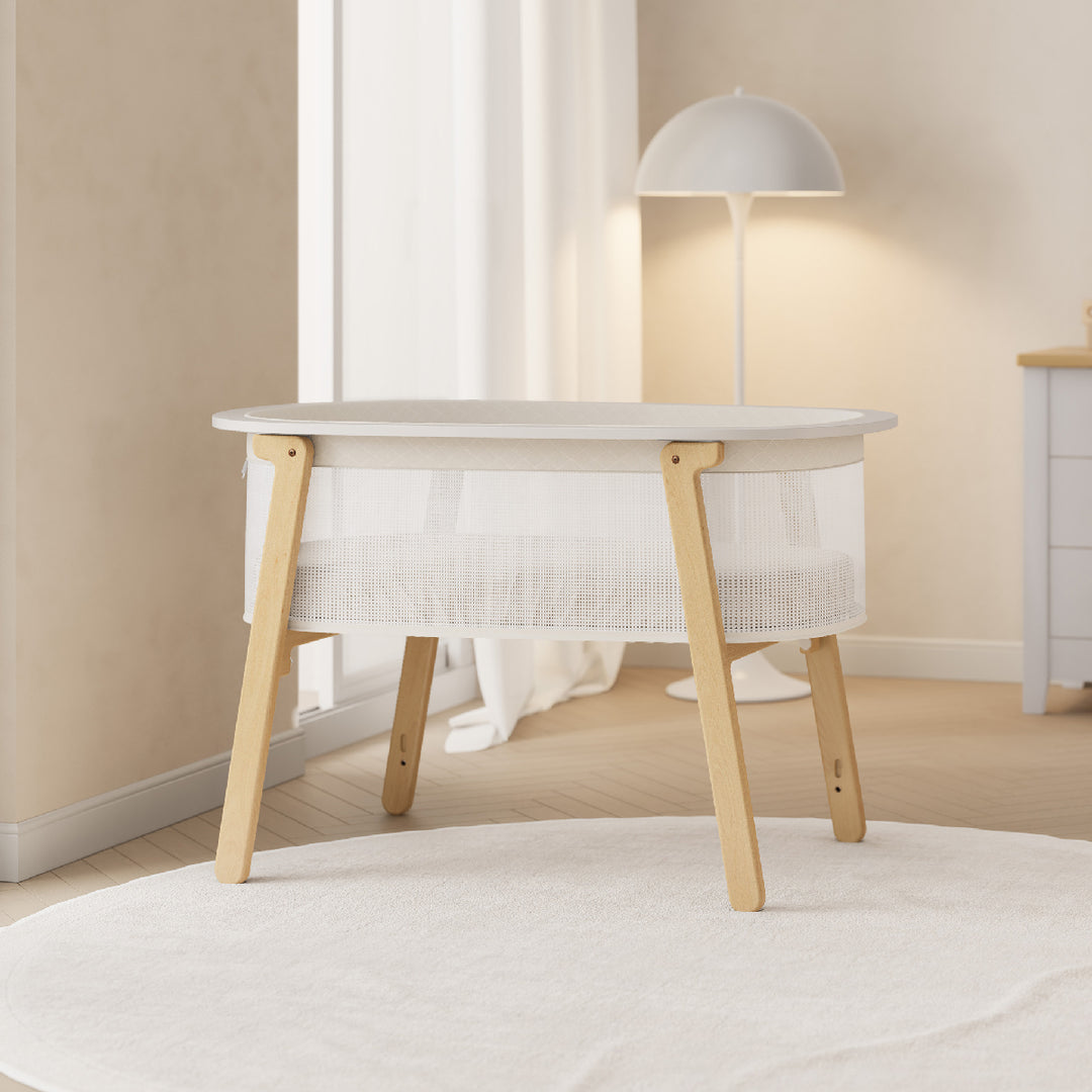 White crib with wooden legs in a room with beige walls and a lamp.