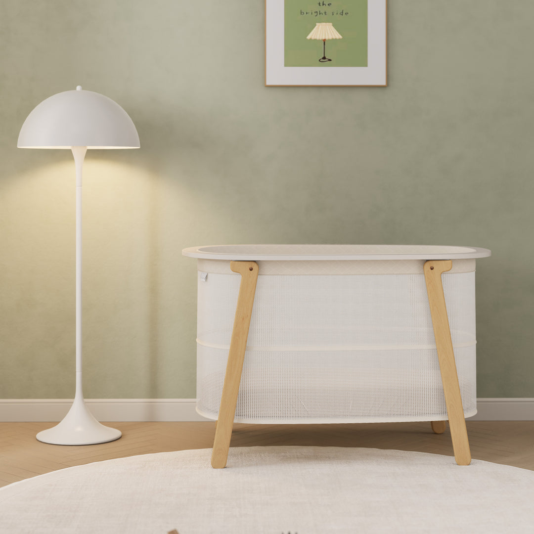 White crib with wooden legs in a room with a green wall and white floor lamp.