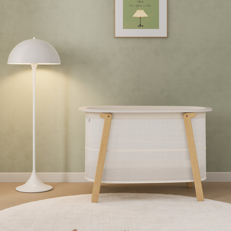 White crib with wooden legs in a room with a green wall and white floor lamp.