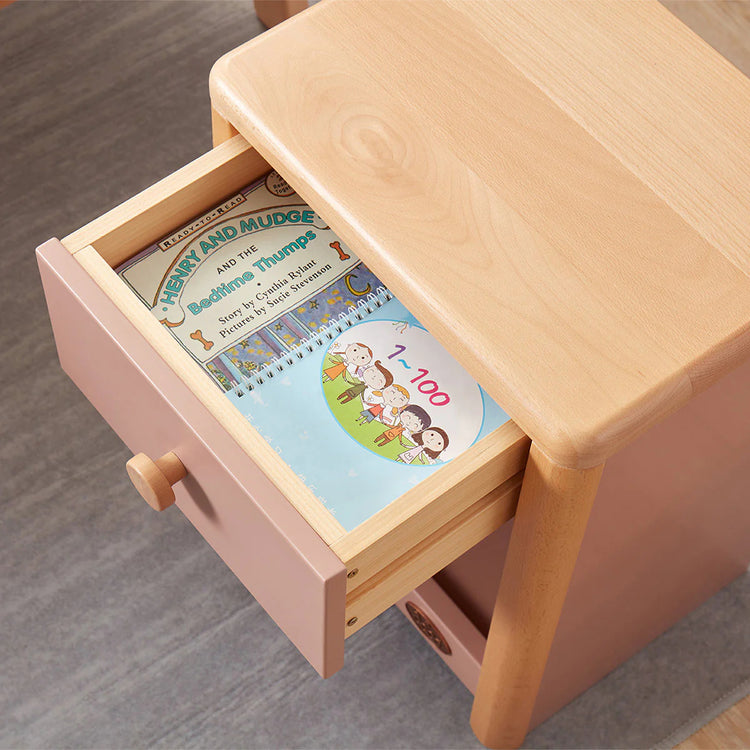 Wooden step stool with open drawer revealing children's books on a gray floor.