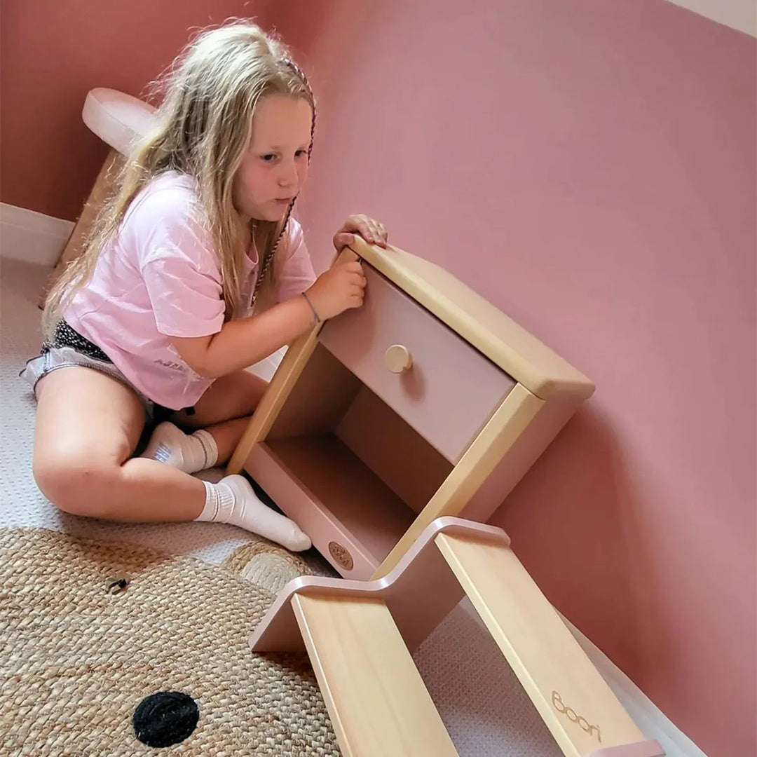 Young girl playing with a pink and gold toy structure against a pink wall.