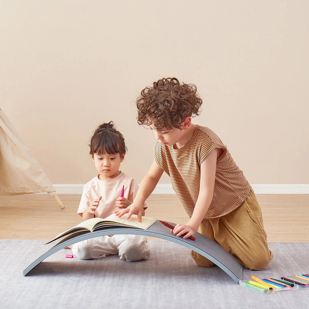 Two children playing with a large open book on the floor.