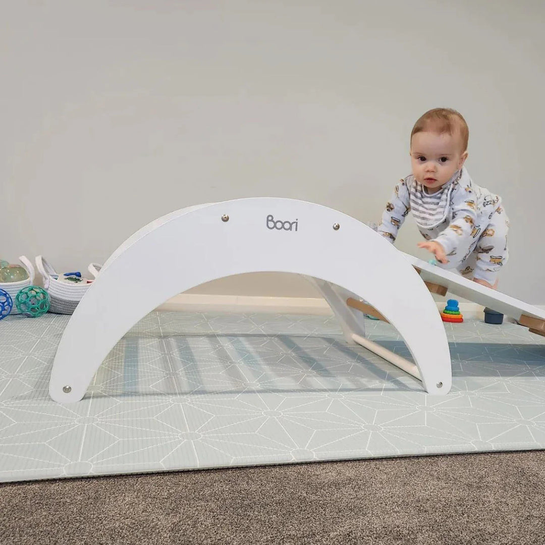 Baby playing with a white play gym on a carpeted floor.