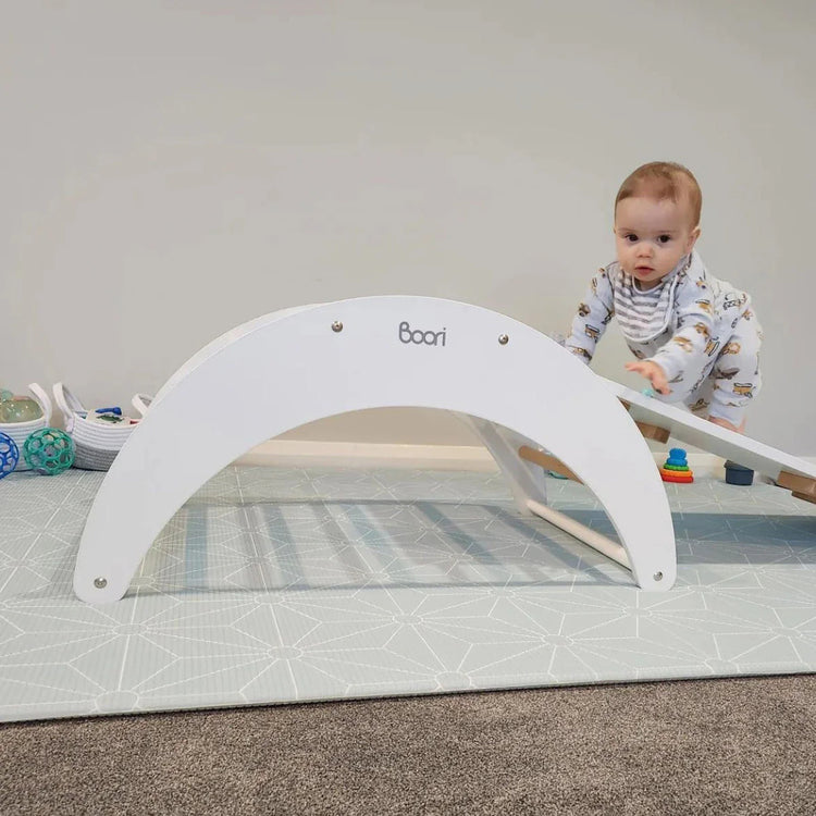 Baby playing with a white play gym on a carpeted floor.