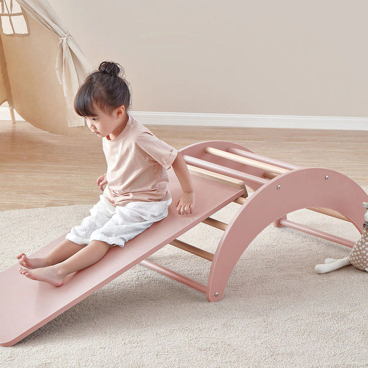 Child playing on a pink wooden seesaw indoors