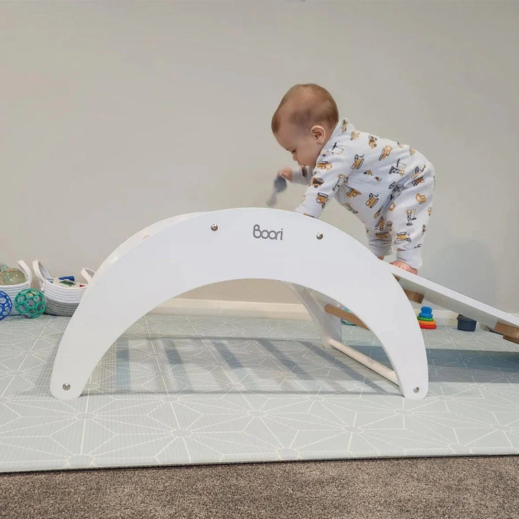 Child playing with a white arch-shaped toy on a tiled floor.