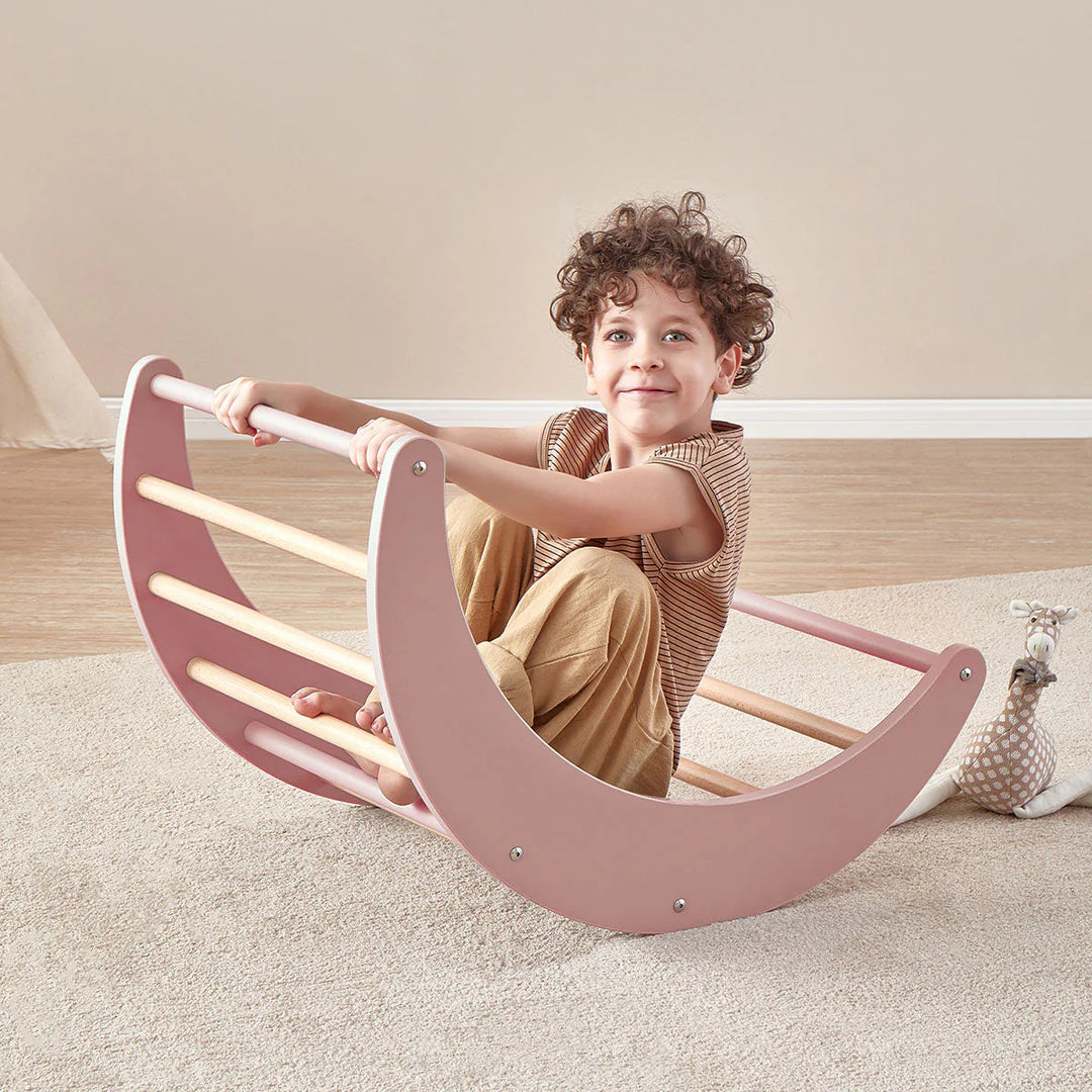 Child sitting on a pink and beige rocking toy in a room with a neutral color scheme.