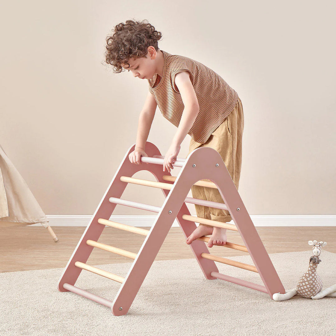 Child climbing a pink and wooden ladder on a light-colored floor.