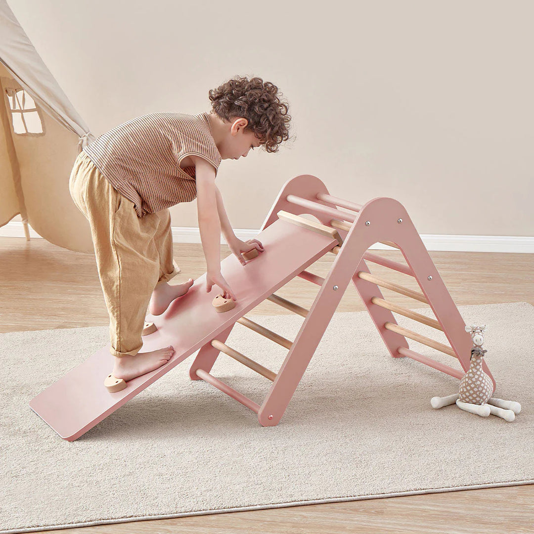 Child playing on a pink and wooden slide indoors