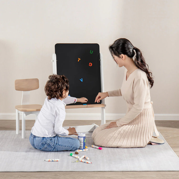 Woman and child playing with a blackboard and colorful magnets on a light-colored floor.