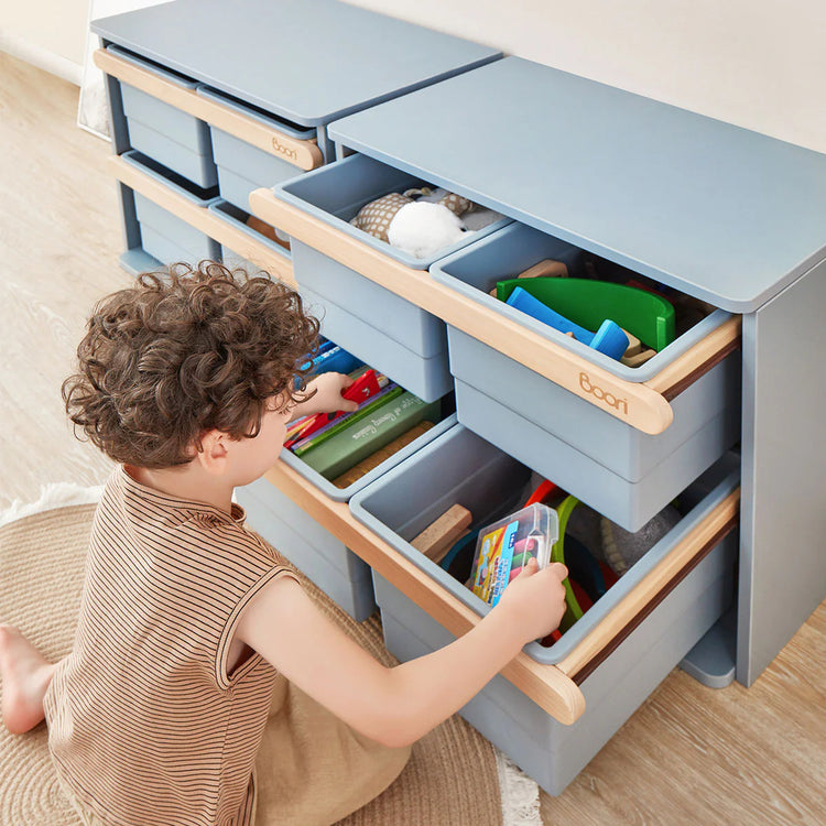 Child interacting with a toy storage unit with multiple drawers.