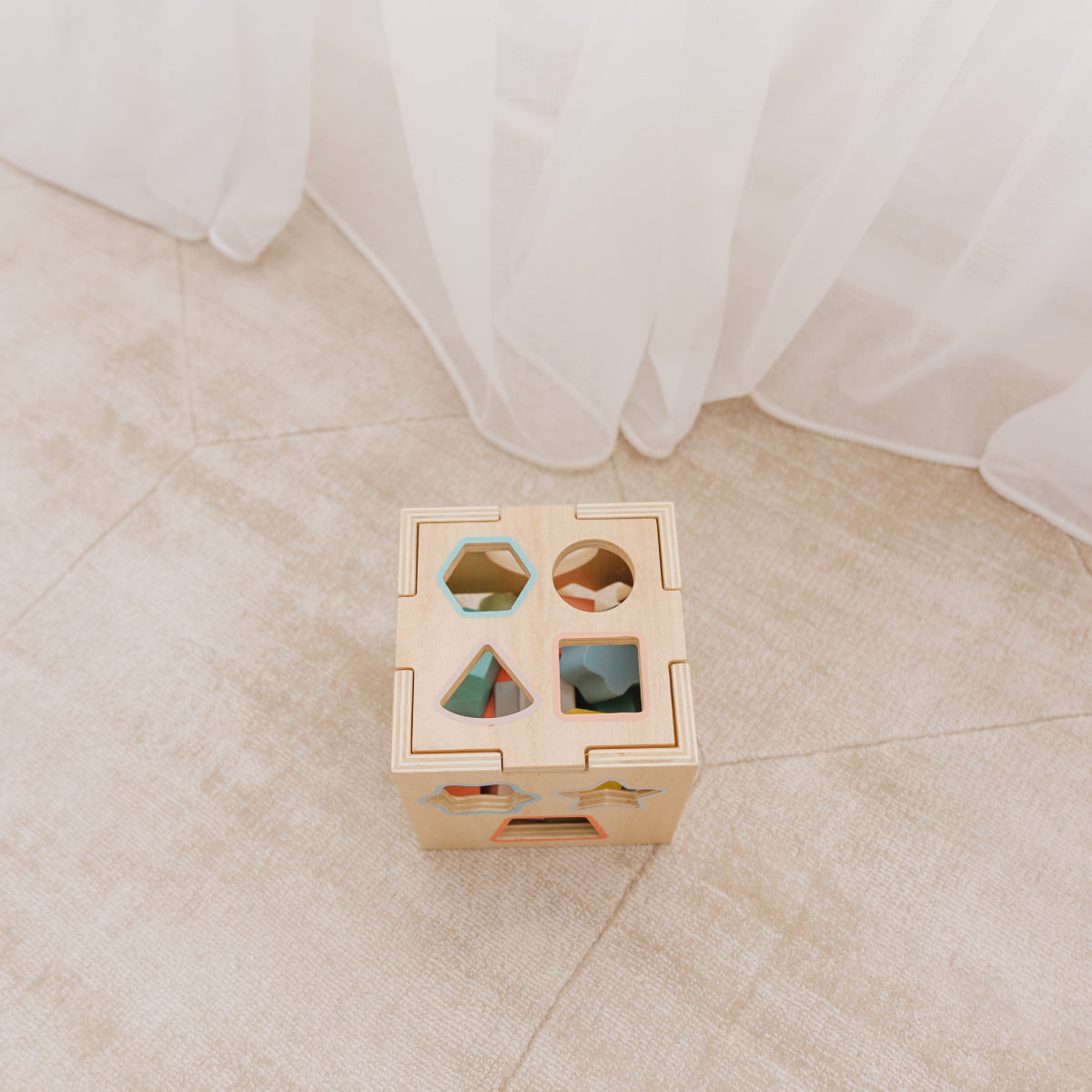 Wooden shape sorting cube on a light wooden floor with white curtains in the background