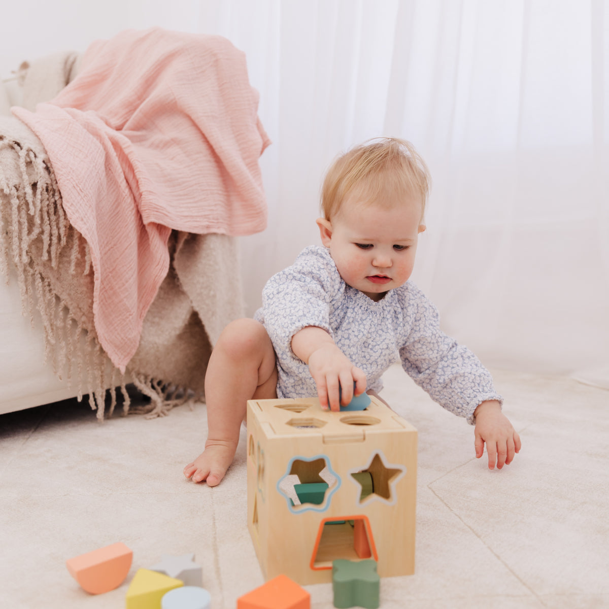 Baby playing with a wooden shape sorter toy on a light-colored floor.