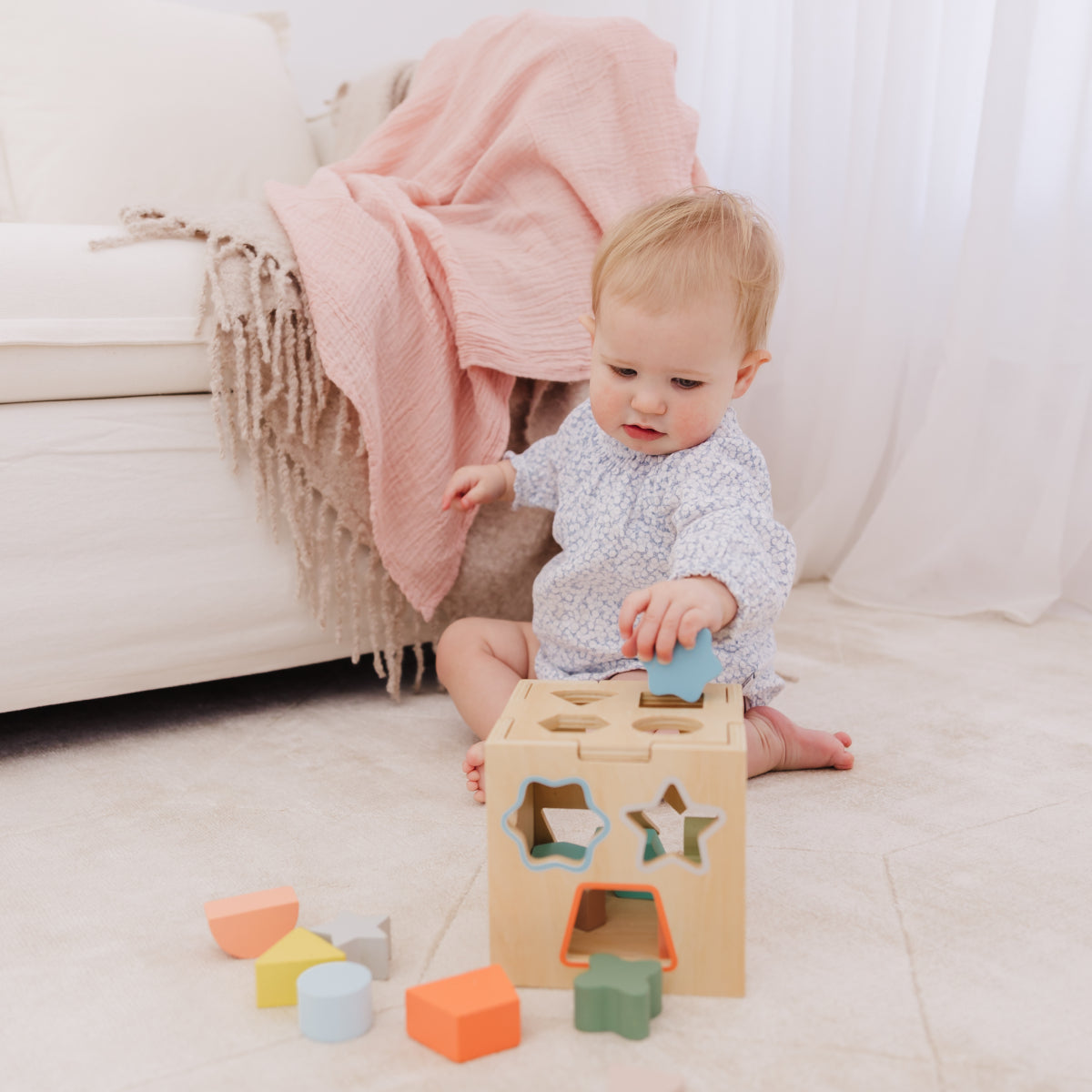 Baby playing with a wooden shape sorter toy on a light-colored floor.