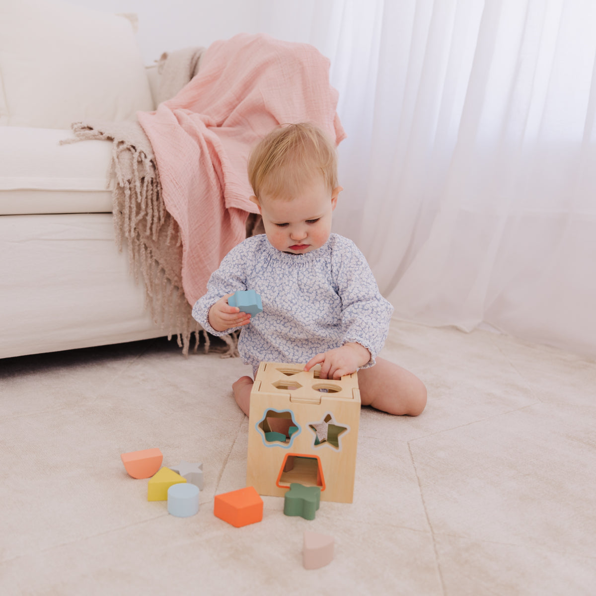 Child playing with a wooden block toy on a light-colored floor.