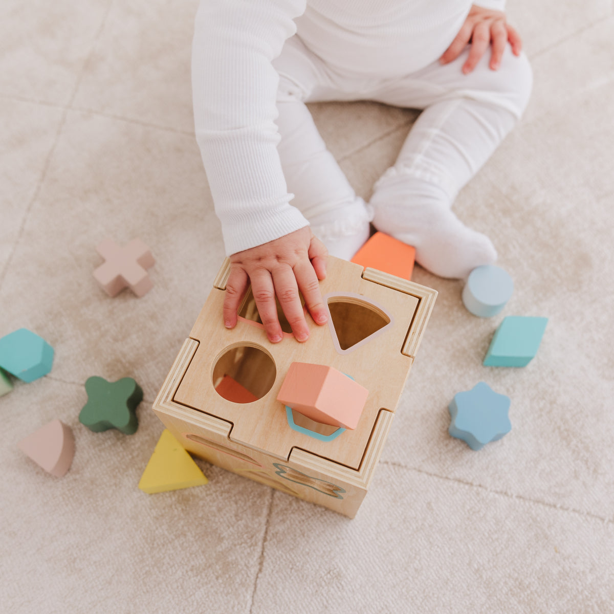 Child playing with a wooden shape sorting toy on a carpeted floor.