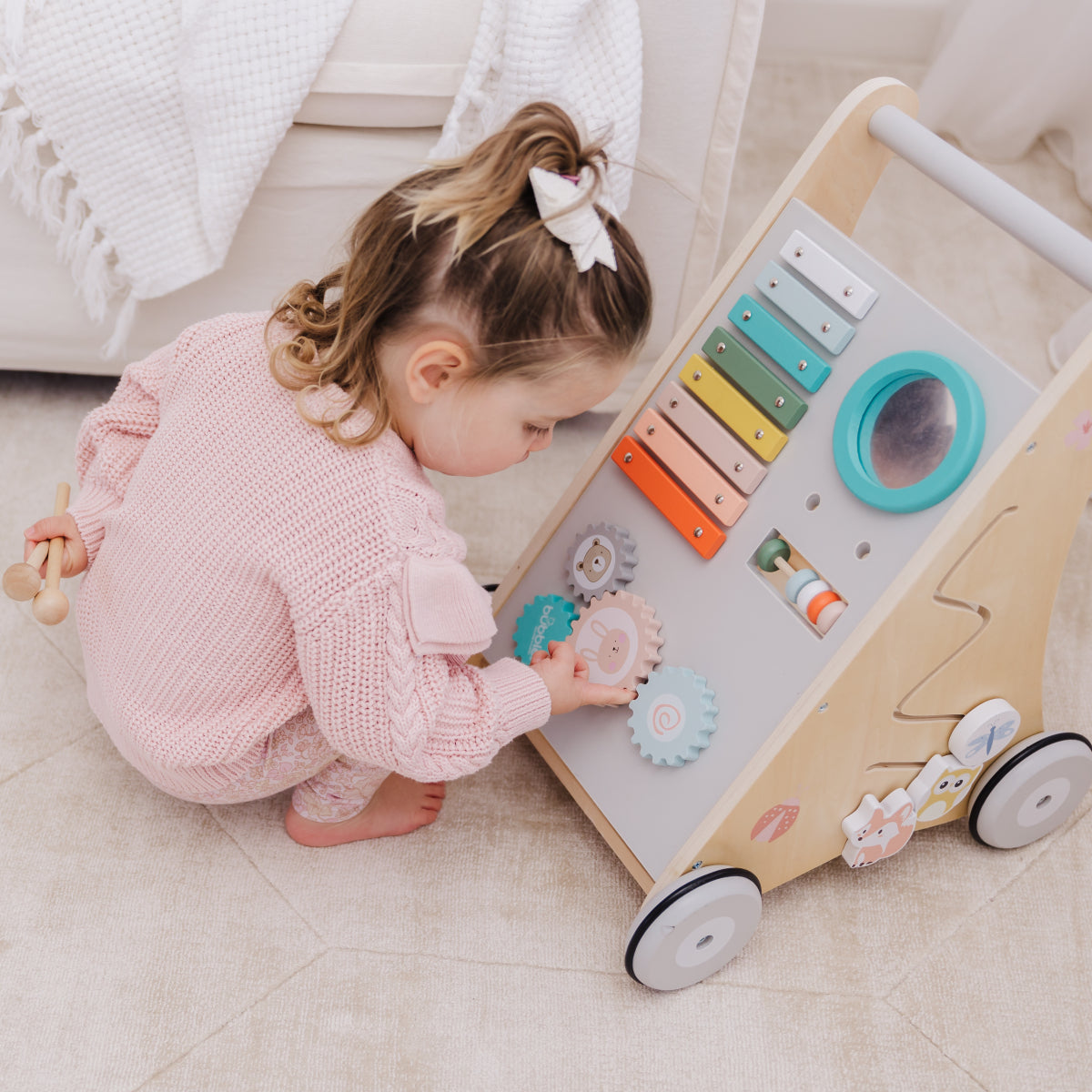 Child playing with a wooden activity center on a light-colored floor.