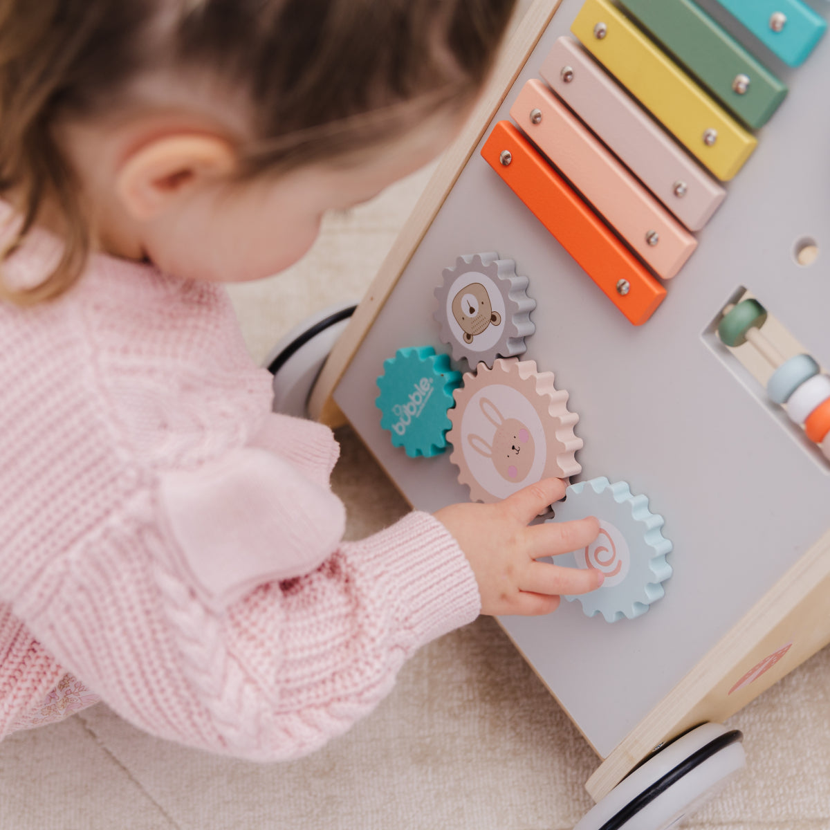 Child playing with a colorful toy xylophone and educational gears on a light surface.